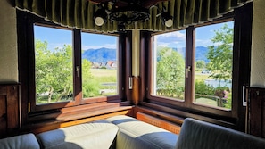 A room with a large window overlooking a green landscape and mountains.