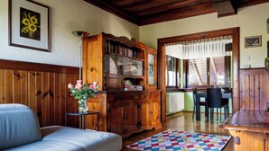 Una sala de estar acogedora con un sofá, un aparador de madera con puertas de vidrio, un comedor con mesa y sillas, y una alfombra colorida.