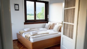 Un dormitorio con una cama de madera, una ventana con vistas a la vegetación y una puerta blanca.