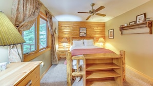 Une chambre confortable avec un lit en bois, une table de chevet avec une lampe, une fenêtre avec des rideaux et un ventilateur de plafond.