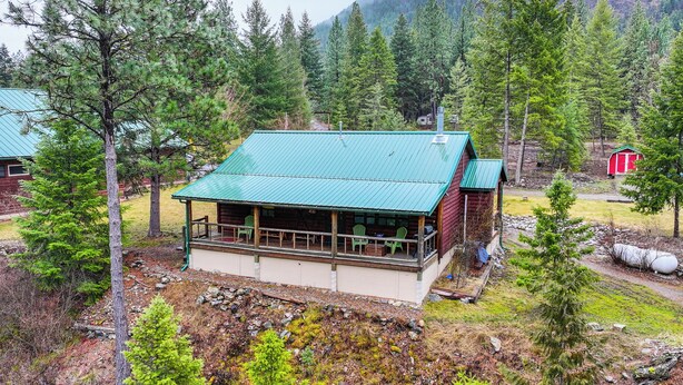 Une cabane surmontée d’un toit végétalisé, entourée d’une forêt dense et de montagnes.