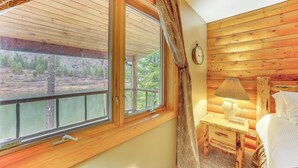 Une chambre dans un chalet en bois, avec une grande fenêtre, une table de chevet avec une lampe et un lit.