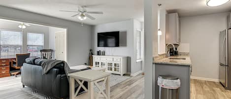 A modern apartment with a living room, kitchen, and dining area. It includes a sofa, dining table, and a TV mounted on the wall.