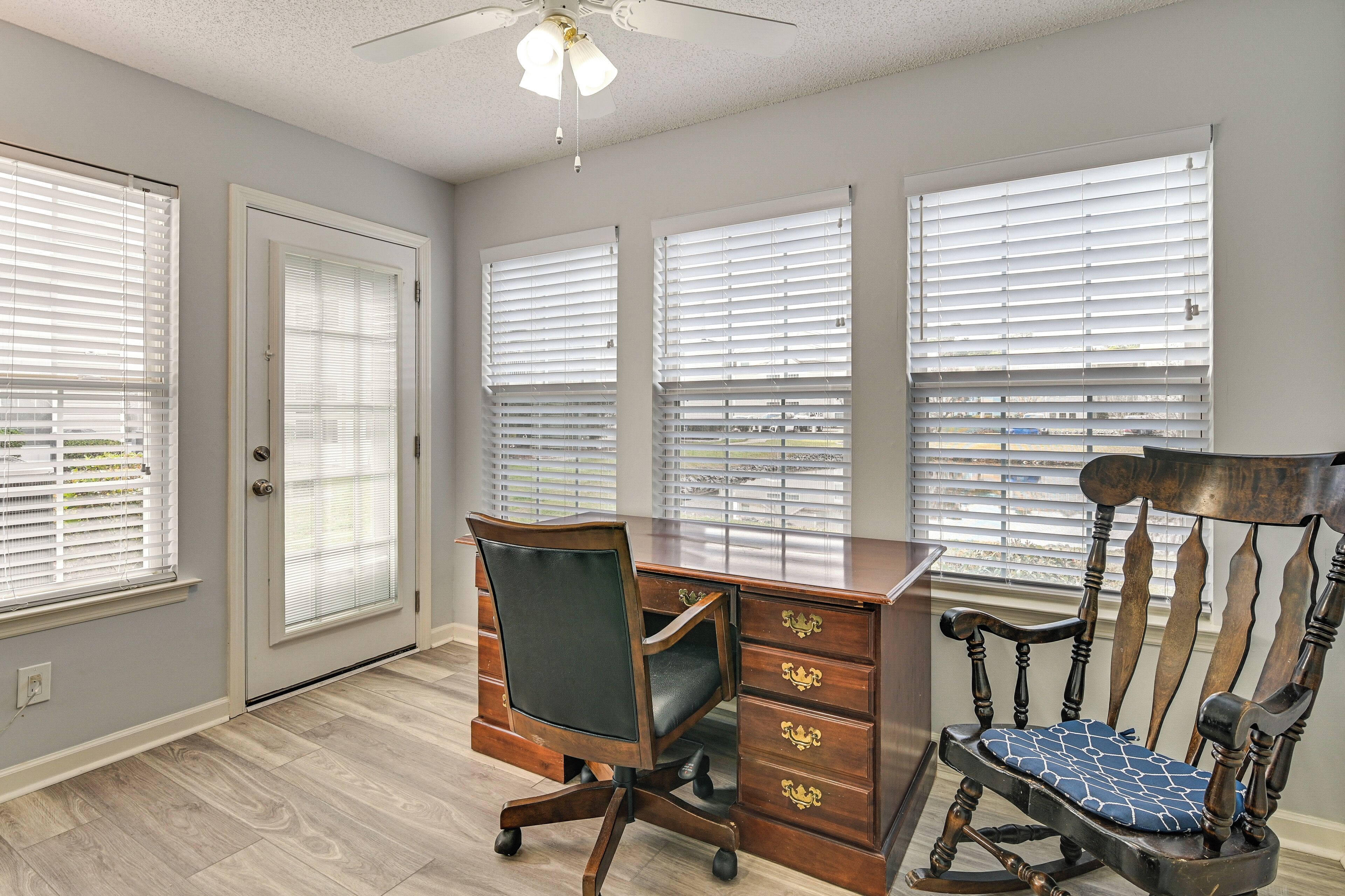 A room with a desk, two chairs, and three windows with blinds.
