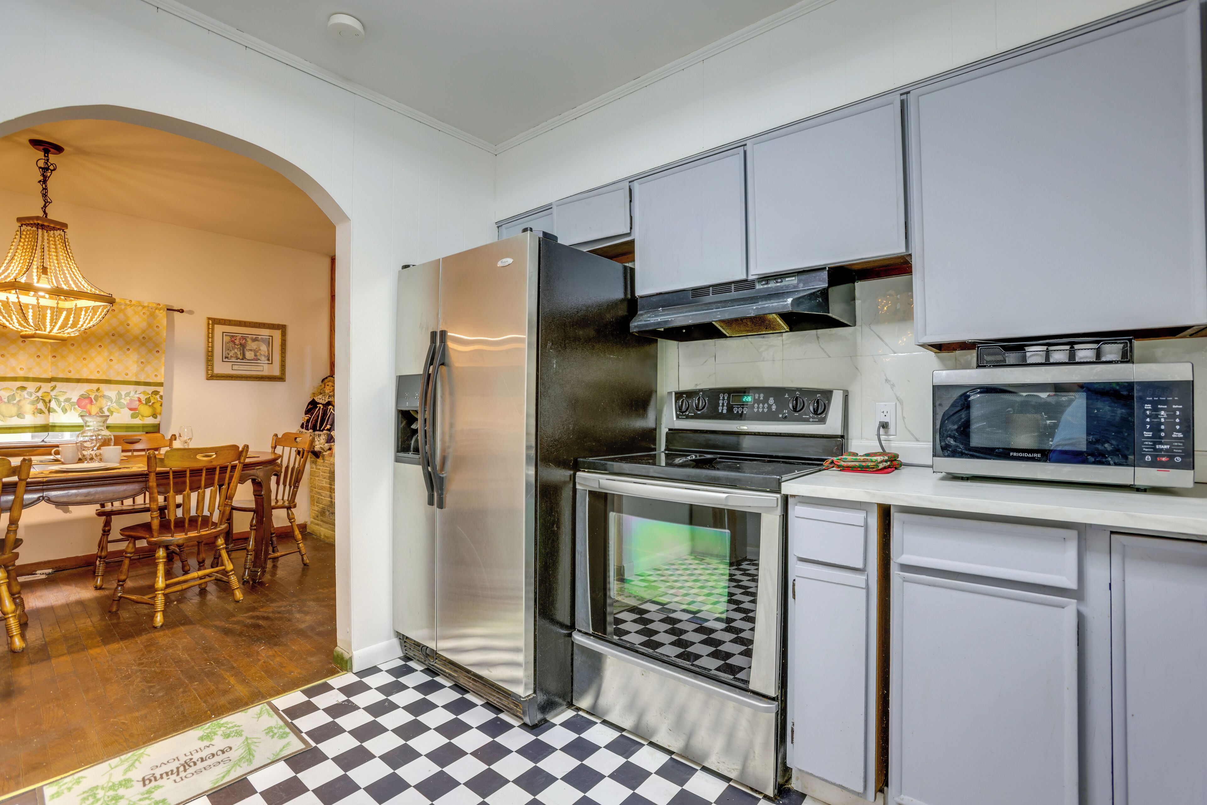 Una cocina equipada con refrigerador, estufa, microondas y un comedor con sillas de madera y candelabro.