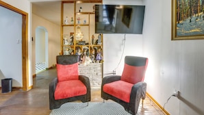 A living room with two armchairs, a TV, a fireplace with figurines, and a painting on the wall. - Pool Table & Shared Sauna! Potomac River Basecamp (Westernport)