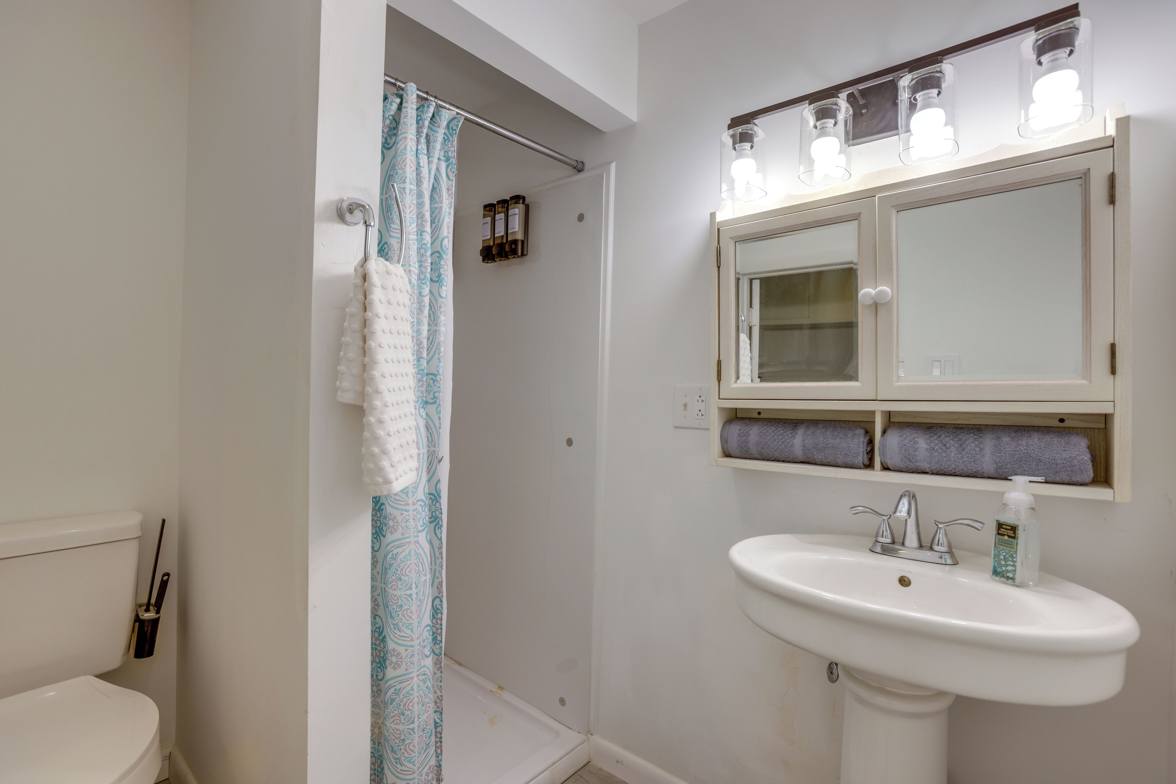 A bathroom with a toilet, shower curtain, sink, and mirror.