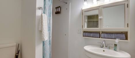 A bathroom with a toilet, shower curtain, sink, and mirror.