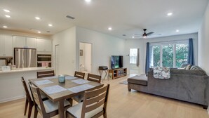 A modern kitchen with stainless steel appliances, a dining area with wooden furniture, and a living room with a grey sofa and a television. - Beach, Eats, Shops! Sunny Stay By European Village (Palm Coast)