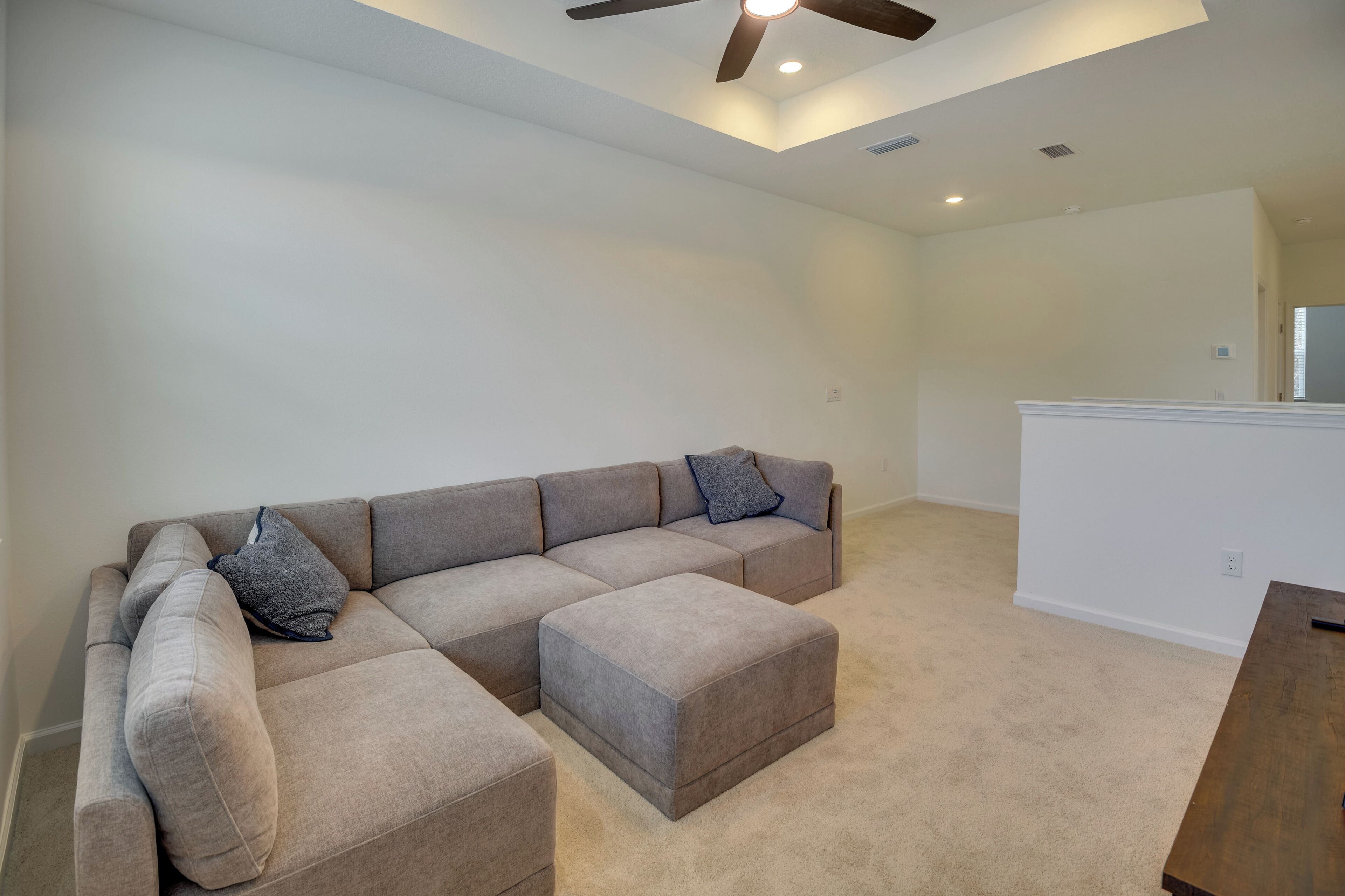 A spacious living area with a sectional sofa and ottoman, a wooden table, and a ceiling fan.
