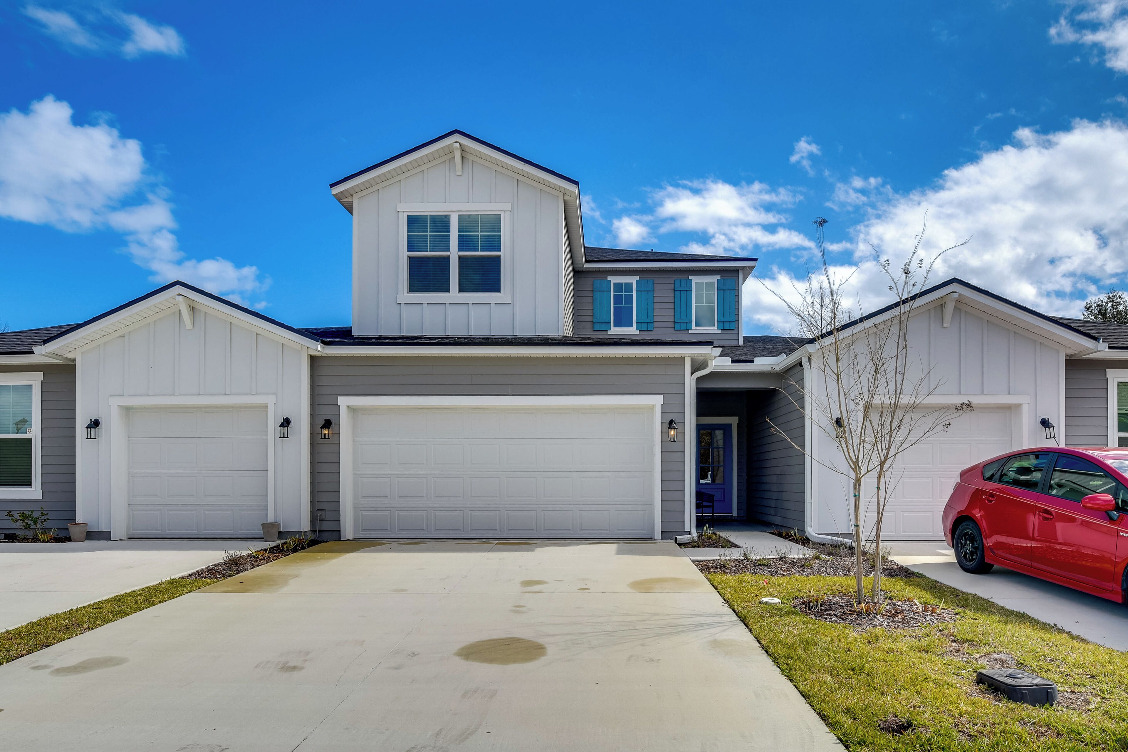 A two-story house with a garage, a driveway, and a red car parked in the driveway.