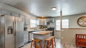 A kitchen with a central island, two stools, stainless steel appliances, and wooden cabinetry. - Mountain Basecamp Near Red Rocks (Golden)