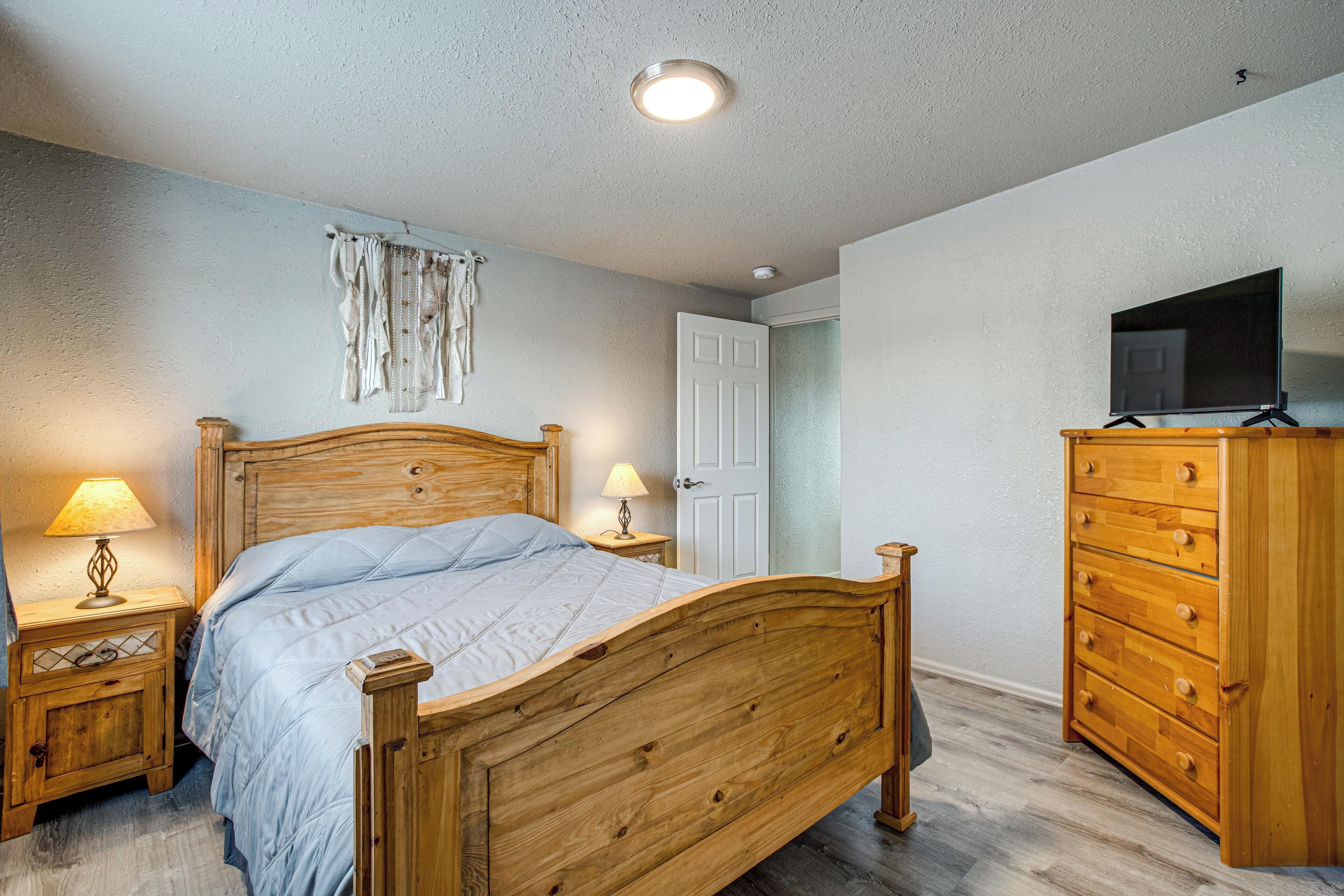 A bedroom with a wooden bed, bedside lamps, a dresser, and a television on a stand.