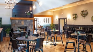 A restaurant with a stone fireplace, wooden beams, and round tables with chairs.