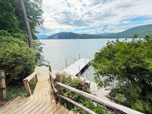 Un pontile di legno che si estende sull'acqua, circondato da vegetazione e colline sullo sfondo.