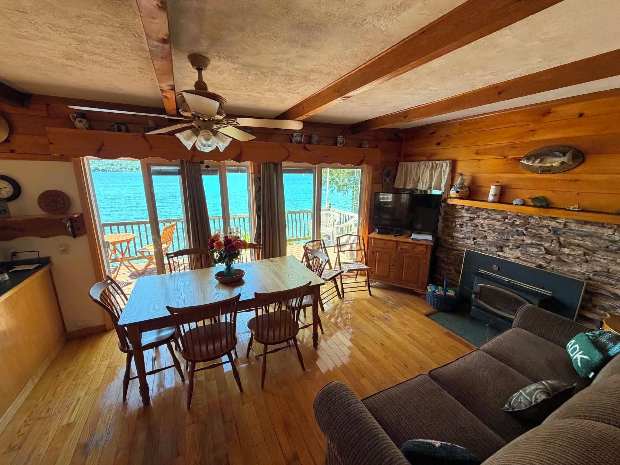 A wooden interior with a dining area, kitchen, and seating by a large window overlooking water.