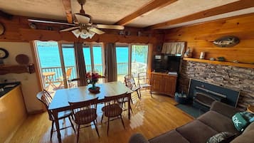 A wooden interior with a dining area, kitchen, and seating by a large window overlooking water.