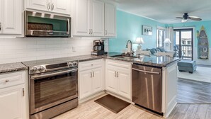 A kitchen with white cabinets, stainless steel appliances, a granite countertop, and a view to the living area. - Golden Mile Getaway Steps From the Beach (Myrtle Beach)