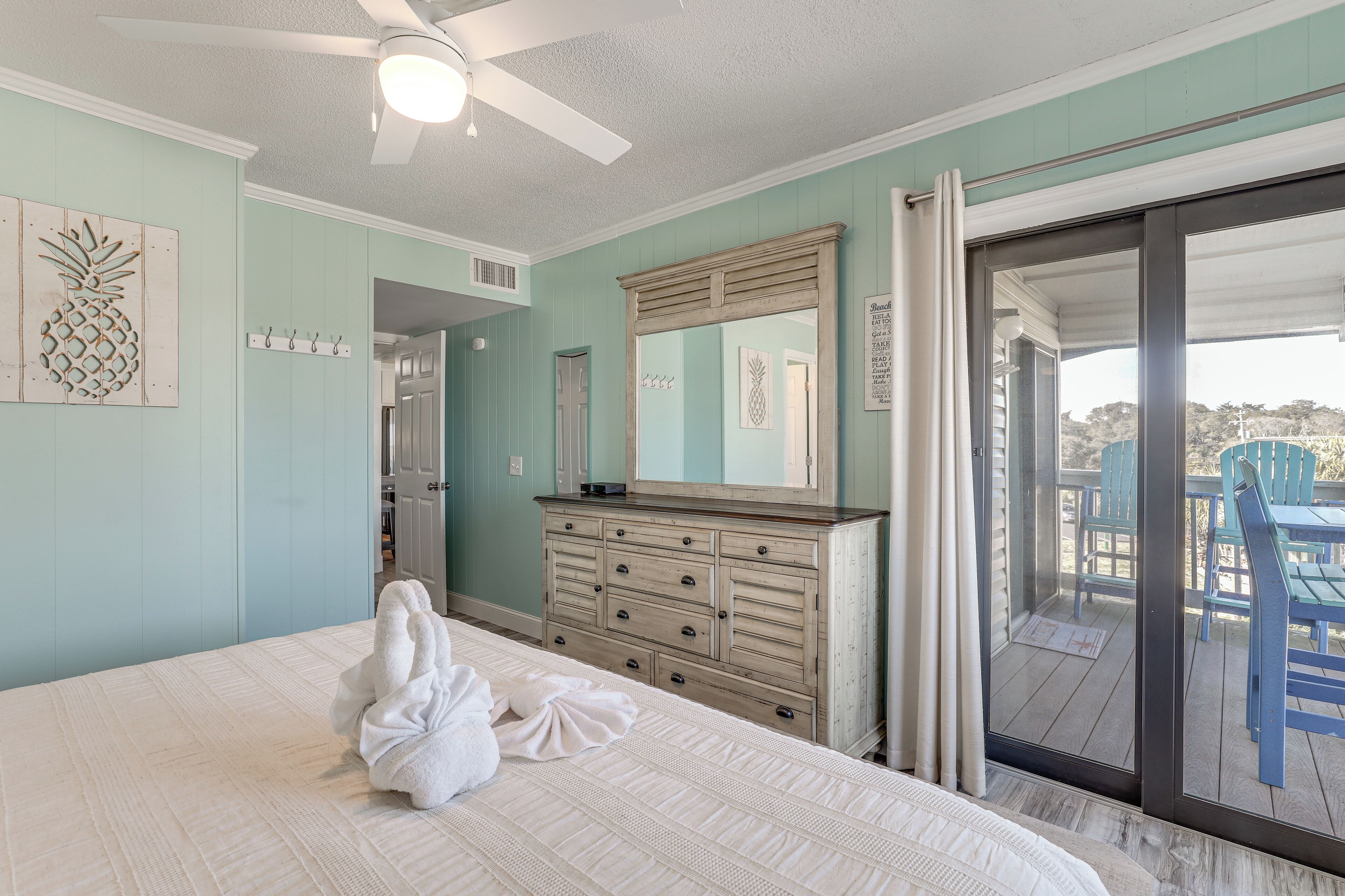 A bedroom with a bed, a dresser, a ceiling fan, a sliding glass door to an outdoor area with chairs.