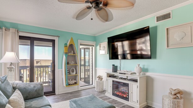 A living room with a sofa, ottoman, fireplace, TV, and a ceiling fan. - Golden Mile Getaway Steps From the Beach (Myrtle Beach)