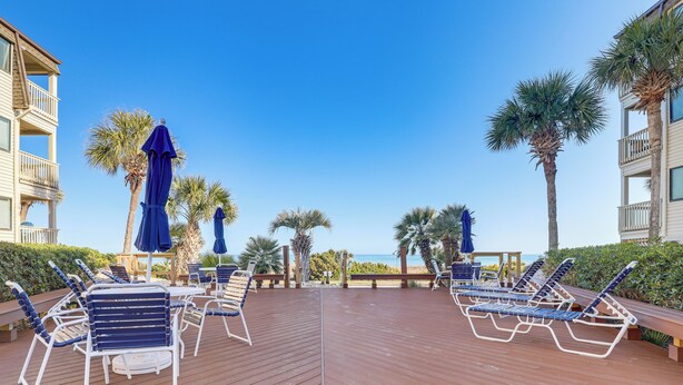 A wooden deck with lounge chairs and umbrellas, overlooking a beach and palm trees. - Steps to Sand! Pool-view Retreat in Myrtle Beach (Myrtle Beach)