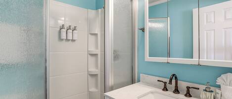A bathroom with a shower, a sink with a mirror, and toiletries on the wall.