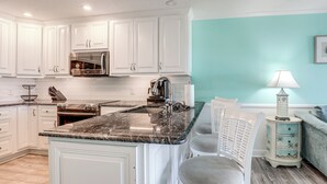 A kitchen with white cabinets, a marble countertop, and a sink. There is a chair and a small table with a lamp. - Steps to Sand! Pool-view Retreat in Myrtle Beach (Myrtle Beach)