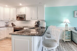 A kitchen with white cabinets, a marble countertop, and a sink. There is a chair and a small table with a lamp. - Steps to Sand! Pool-view Retreat in Myrtle Beach (Myrtle Beach)