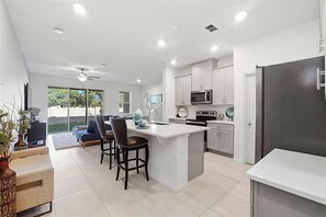 Una cocina moderna con armarios blancos, una isla central y un comedor con sillas.