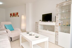 A living room with a white sofa, a coffee table, a TV mounted on a white cabinet, and a glass display cabinet with decorative items. - Tucuman 3 Los Huertos Nerja by Casasol (Nerja)