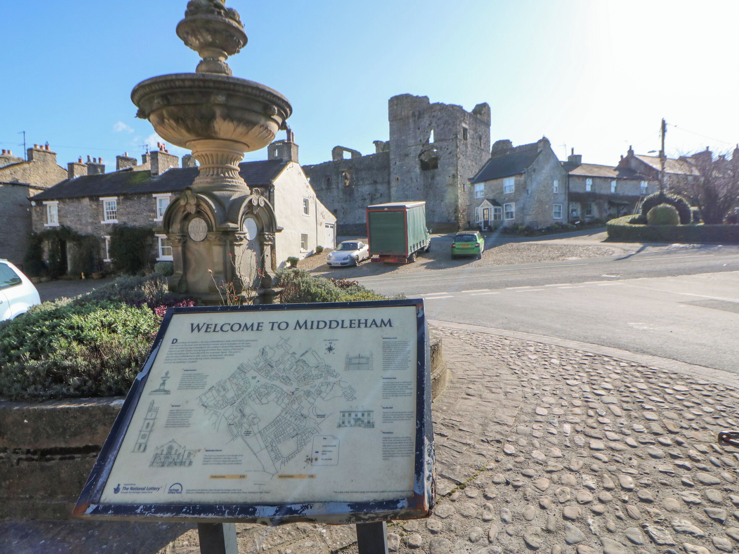 Un cartel de bienvenida con un mapa, un edificio histórico y una fuente de piedra.