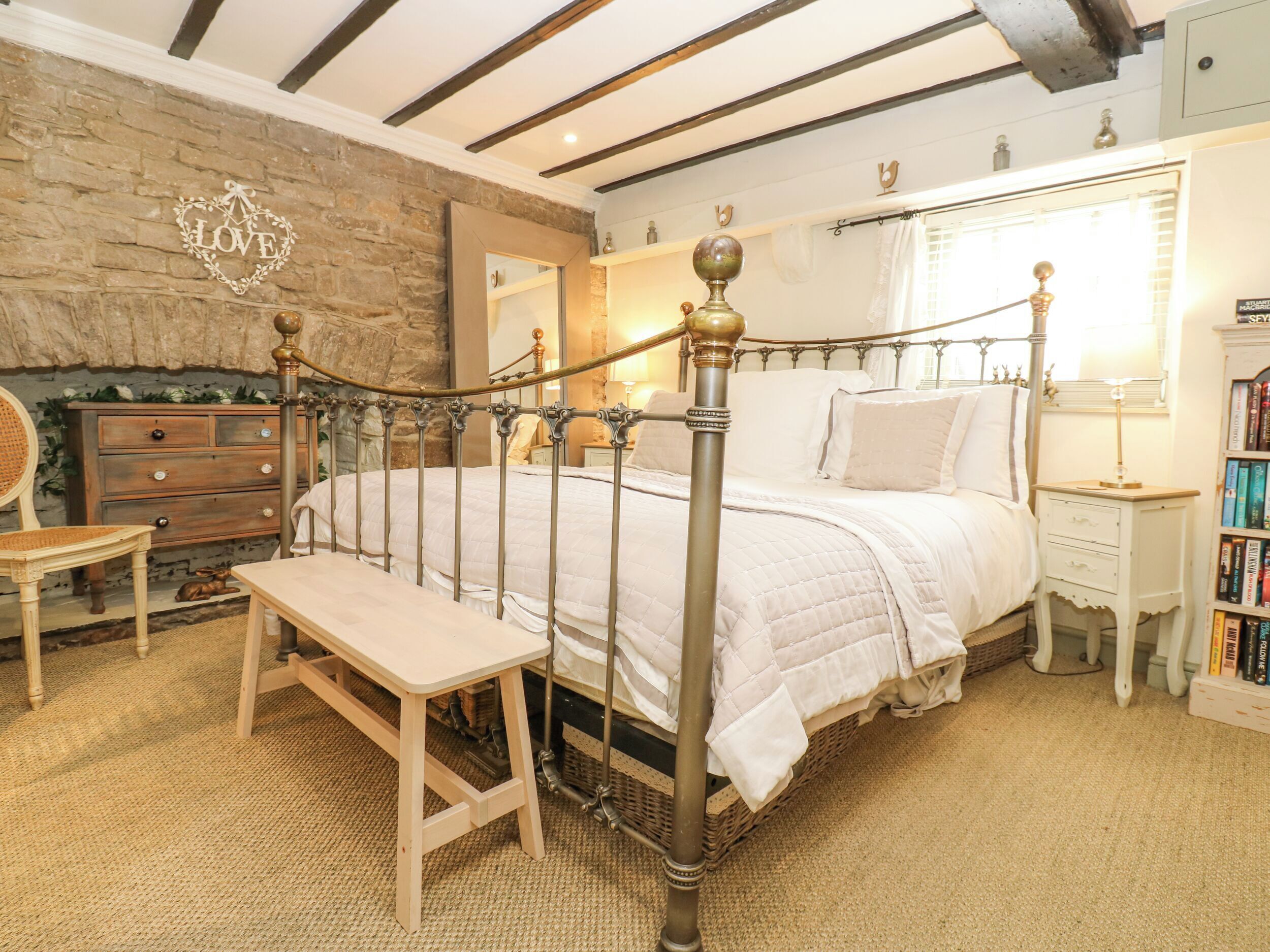 Un dormitorio con cama de dosel, cómoda de madera, banca, estantería y pared de piedra.