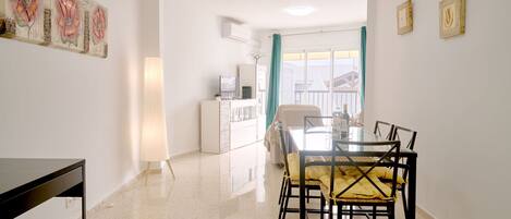 A modern dining area with a glass table and chairs, a white cabinet, and a large window with curtains.