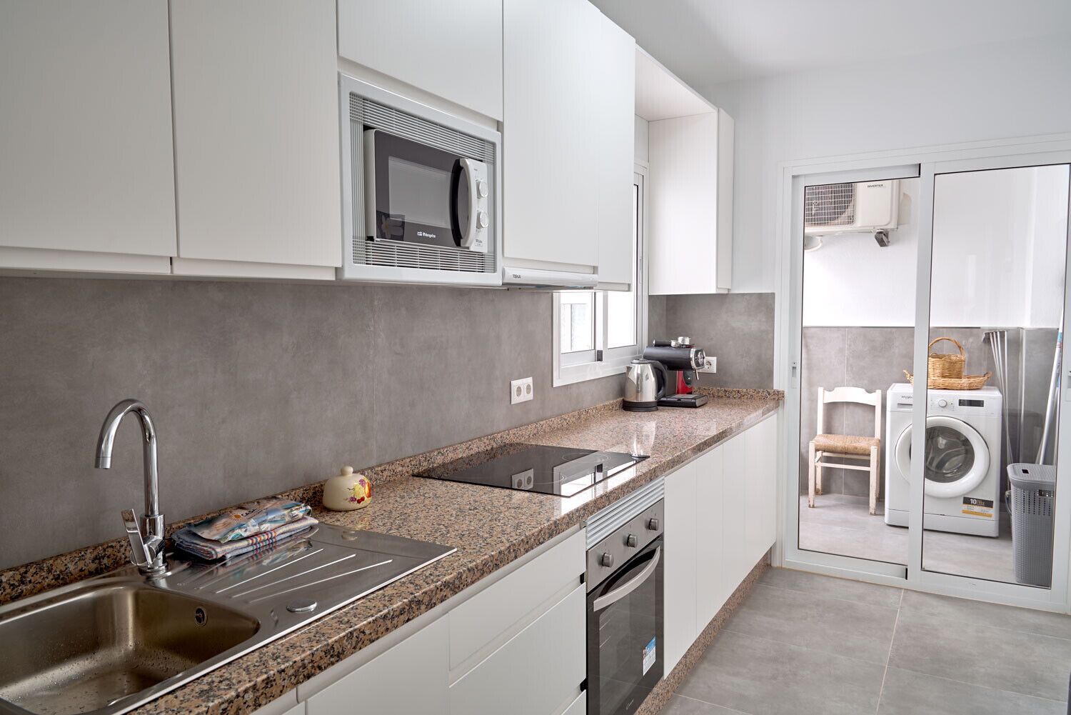 A modern kitchen with white cabinets, a granite countertop, stainless steel appliances, and a built-in washer and dryer.