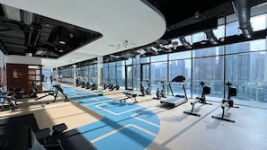 Ein modernes Fitnessstudio mit vielfältigen Trainingsgeräten, großen Fenstern mit Blick auf die Stadt und einem aufgeräumten, großzügigen Design.