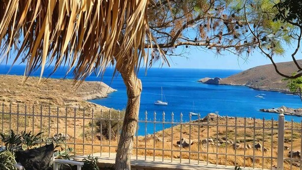 A coastal view with a stone wall, a metal fence, and a thatched roof structure.