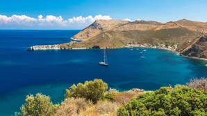 A coastal landscape with clear blue waters, a small island, and a sailboat.