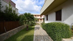 A courtyard with a stone pathway, a palm tree, and a hedge. - Pietra Sole Villa (Makry Gialos)
