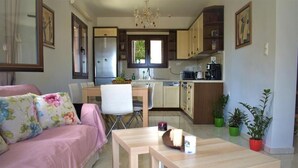 A cozy living room with a pink sofa, a wooden coffee table, and a dining area with a white chair. - Pietra Sole Villa (Makry Gialos)