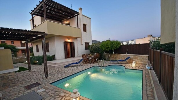 A modern two-story house with a swimming pool, stone patio, and outdoor seating area. - Pietra Sole Villa (Makry Gialos)