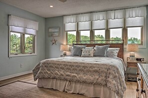 Ein Schlafzimmer mit einem großen Bett, zwei Nachttischen, einem Schminktisch und einem Fenster mit Blick auf Grünflächen.