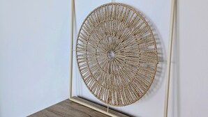 A framed, circular, woven artwork displayed on a wooden cabinet against a white wall.