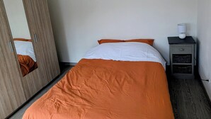 A bedroom with a bed, a wardrobe, a nightstand, and a mirror.