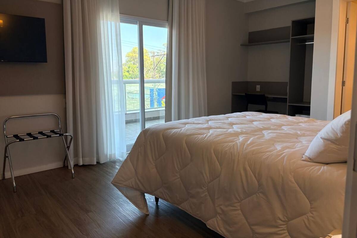 Ein Hotelzimmer mit Bett, Fernseher, einem Balkon mit Vorhängen und einem Kleiderschrank.