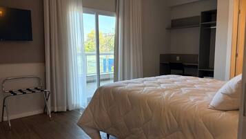 A hotel room with a bed, a TV, a balcony with curtains, and a wardrobe.