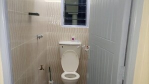 A narrow bathroom with a toilet, a window, and a checkered floor. - White Castle Hotel Mikindani (Mombasa)