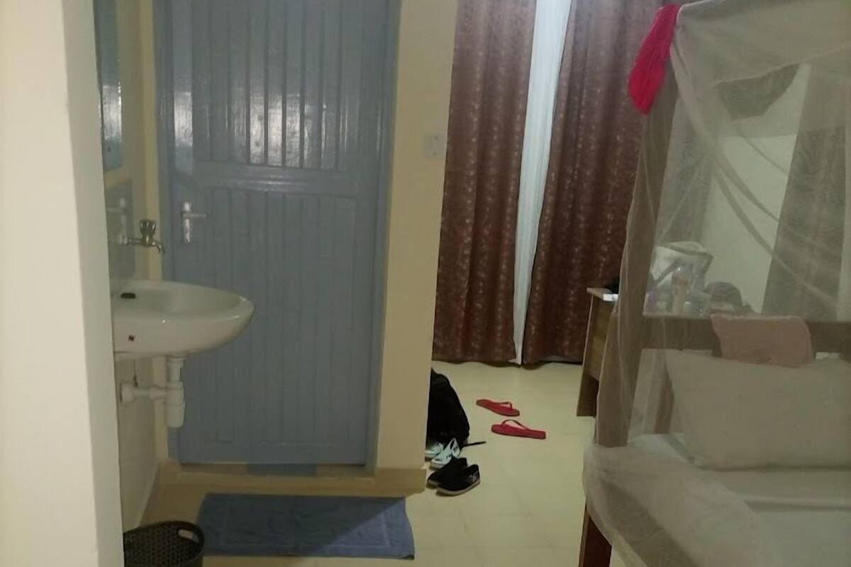 Une chambre à coucher avec un lit, une table de chevet, une fenêtre avec des rideaux, un lavabo et une porte.