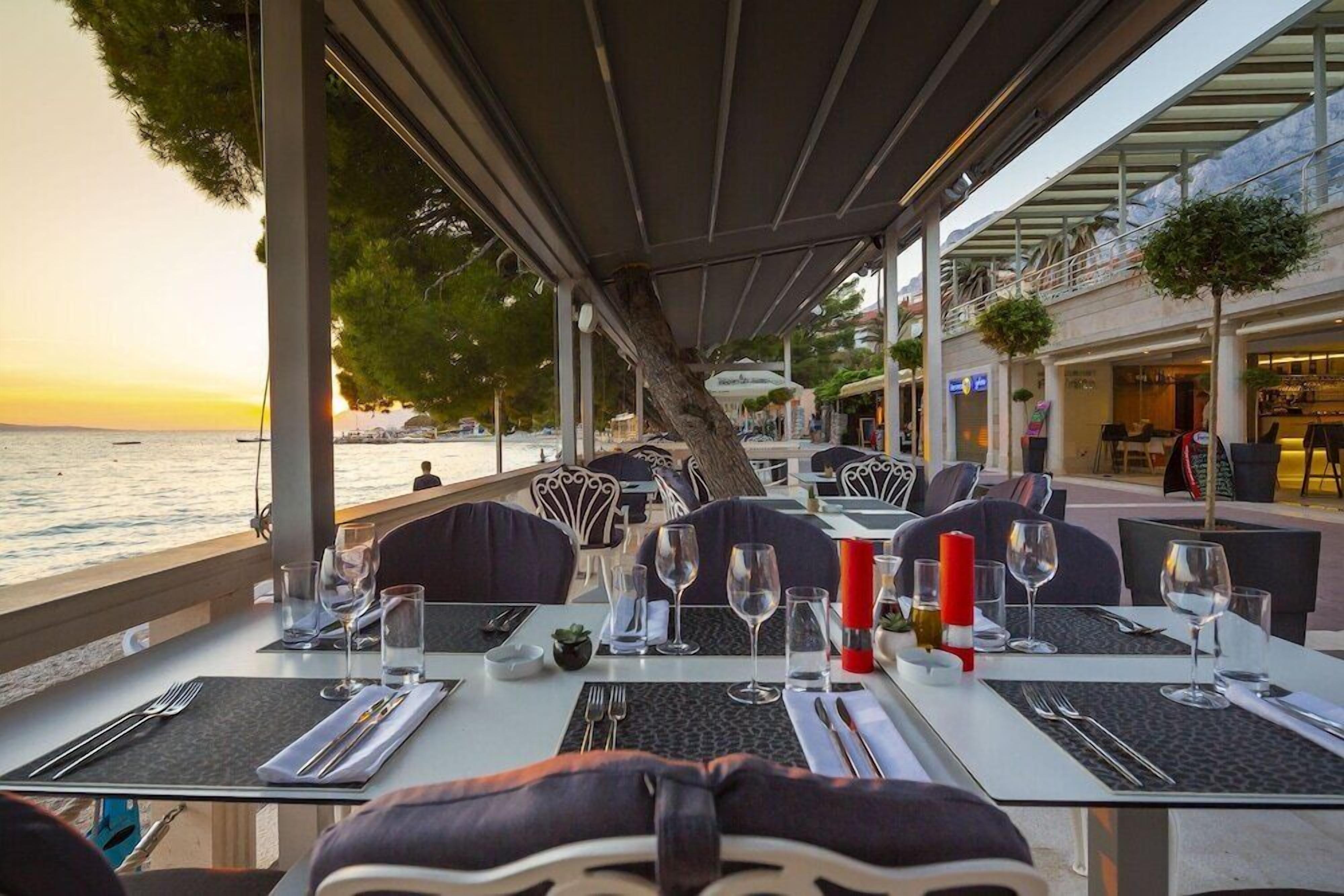 Un espace de restauration en plein air avec des tables disposées pour deux personnes, donnant sur un plan d’eau.