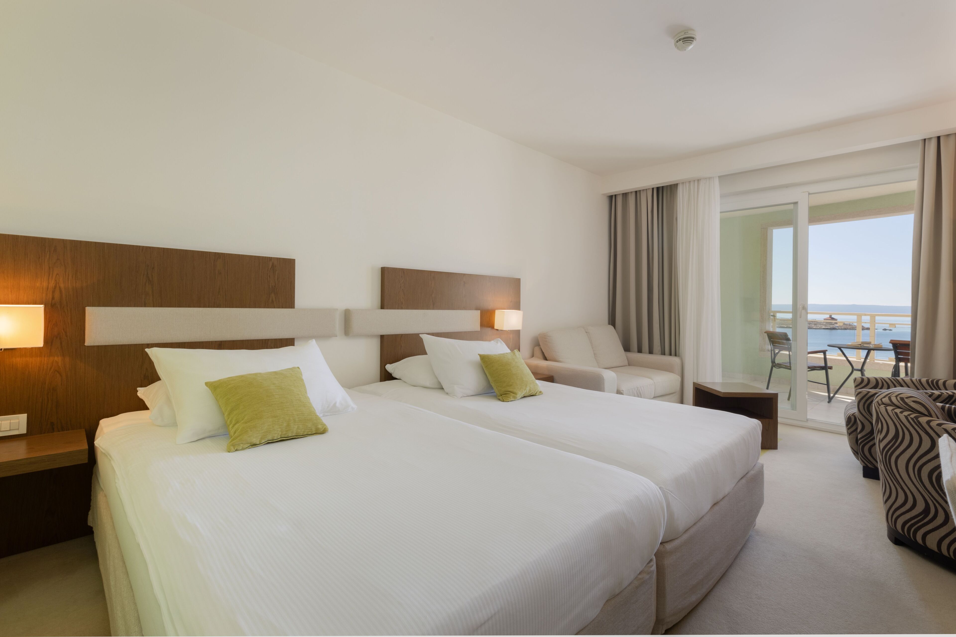 A hotel room with two beds, a sofa, a chair, and a balcony with a view.
