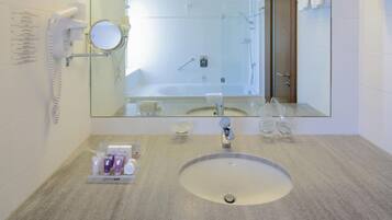A bathroom with a round sink, a mirror, a handheld showerhead, and toiletries.